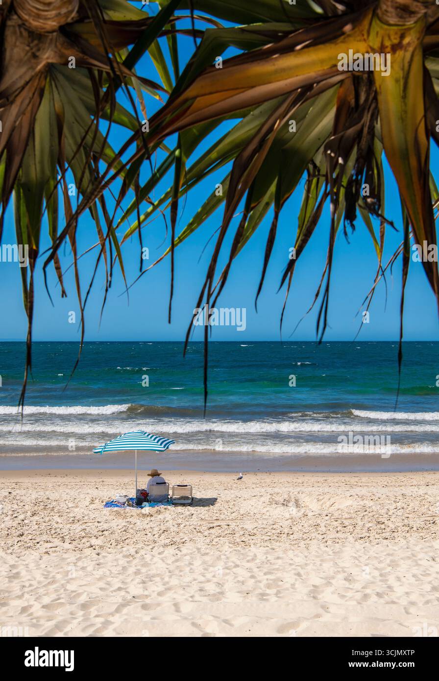 Frau, die am Strand in Noosa Heads/Australien unter dem Sonnenschirm sitzt Stockfoto