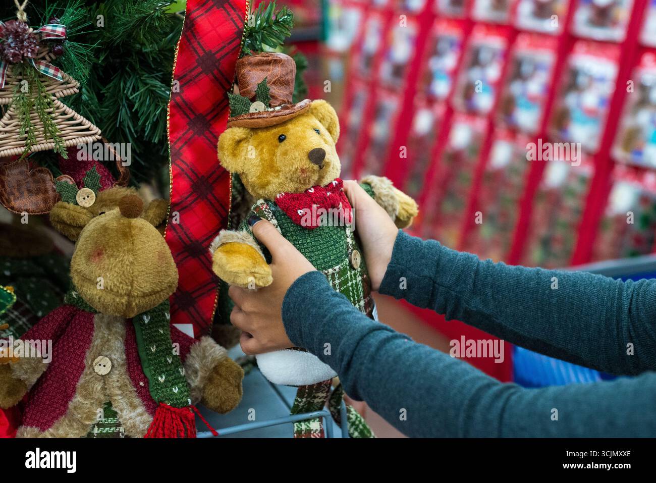 Nahaufnahme der Hände, die sorgfältig einen charmanten Weihnachts-Teddybären in einem Geschäft auswählen Stockfoto