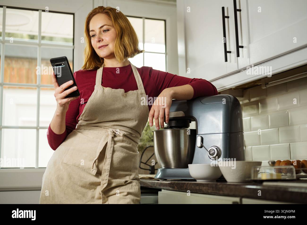 Frau im mittleren Alter Millennial mit Smartphone kochen in der Küche Stockfoto