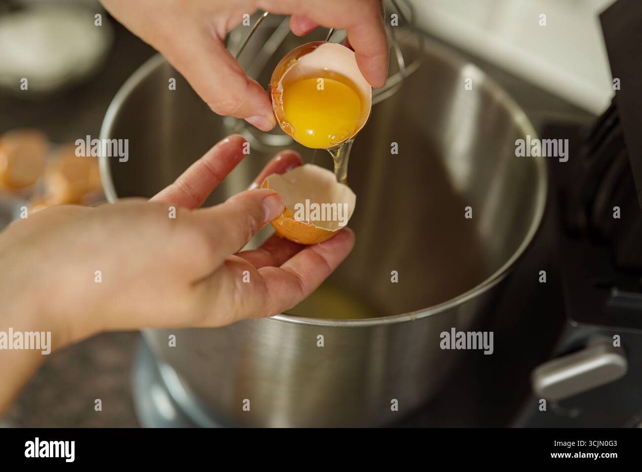 Weibliche Hände brechen das Ei und trennen das Eiweiß vom Eigelb Stockfoto