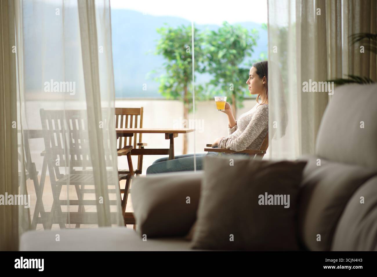 Seitliches Porträt einer Teetrinkenden Frau auf einer Terrasse mit Blick auf zu Hause Stockfoto