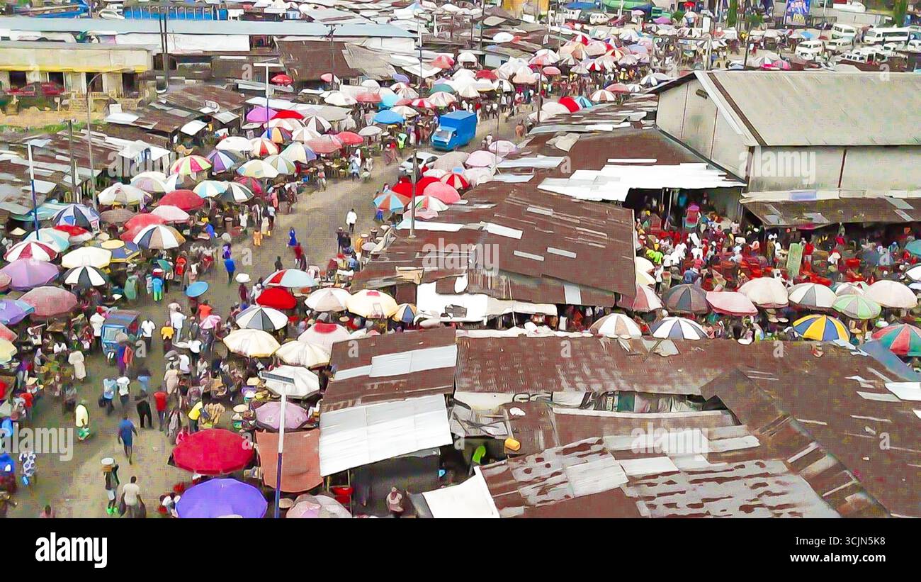 Aus der Vogelperspektive sehen Sie eine geschäftige Marktszene mit pulsierenden Regenschirmen, die Händler und Käufer unter dicht bepackten Ständen beschatten, Elelenwa, Port Harcourt, Nigeria. Stockfoto