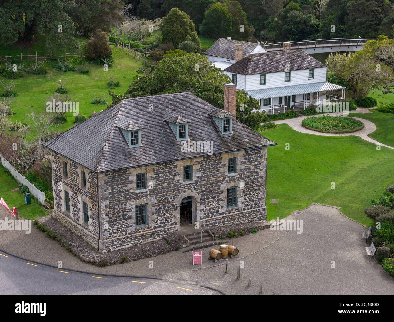 Blick aus der Vogelperspektive auf den Stone Store, ein historisches Gebäude mit grauem Stein und einem dunklen Dach, im Kontrast zum hellen weißen Kemp House, Kerikeri, Northland Region, Neuseeland. Stockfoto