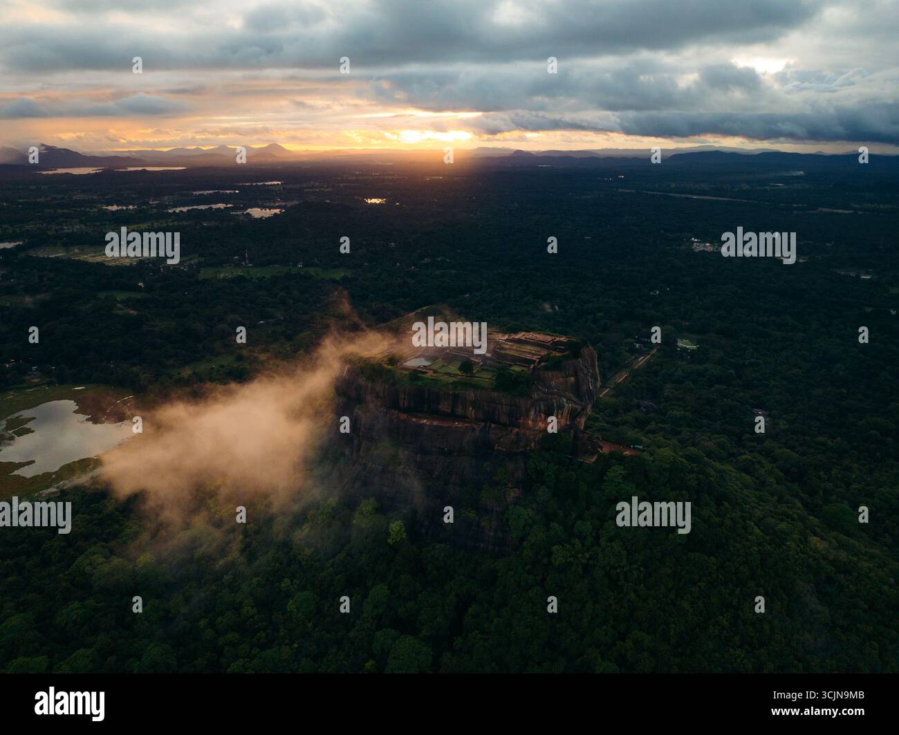 Blick aus der Vogelperspektive auf Sigiriya, eine majestätische Felsenfestung, die durch die grüne Landschaft unter einem dramatischen Sonnenuntergangshimmel durchsticht, Lion Rock, Zentralprovinz, Sri Lanka. Stockfoto