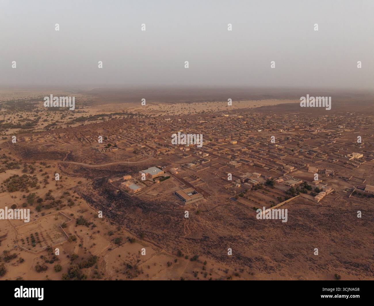 Aus der Vogelperspektive auf die sandigen Farbtöne und die komplizierten Strukturen der antiken Stadt, die sich mit der trockenen Landschaft unter einem trüben Himmel verschmelzen, Ouadane, Adrar, Mauretanien. Stockfoto