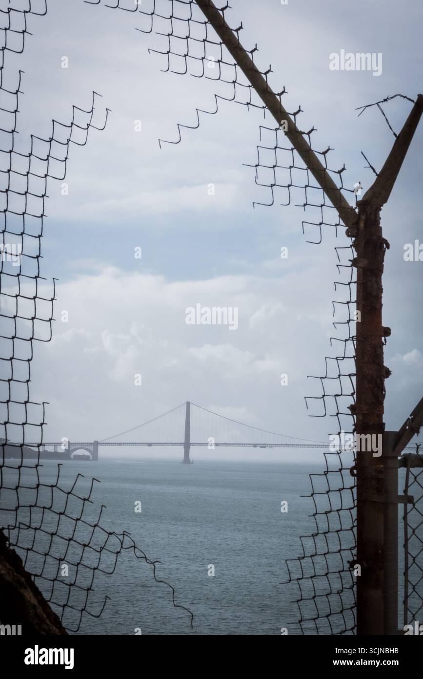 Blick auf die Golden Gate Bridge durch einen zerrissenen Maschendrahtzaun, ein ergreifender Kontrast von Einsamkeit und Freiheit, San Francisco, Kalifornien, USA. Stockfoto