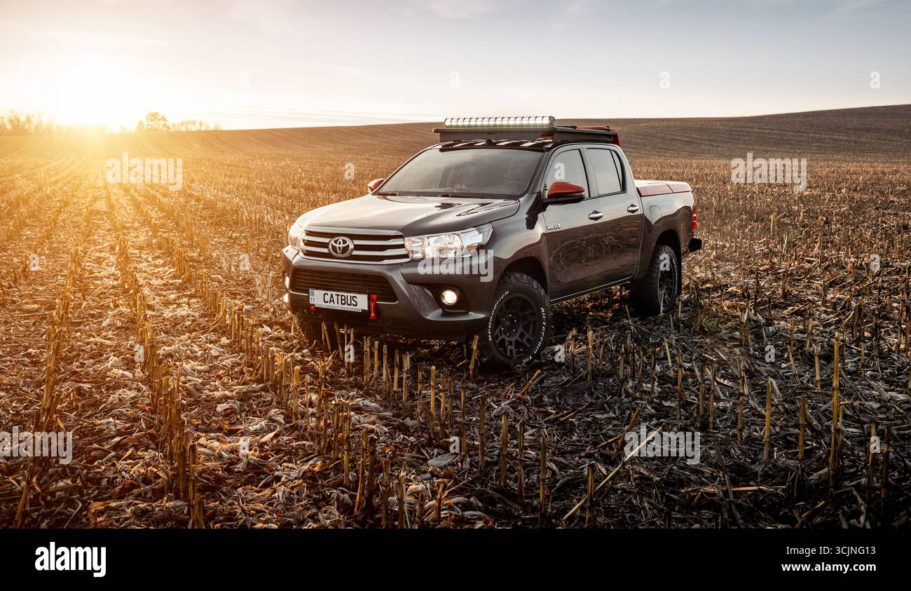 Grauer Toyota Hilux auf trockenem Feld bei Sonnenuntergang. Dreiviertel-Frontansicht des Toyota Pickup-Trucks mit Doppelkabine mit Dachträger und Lichtleiste auf einem geernteten Feld Stockfoto