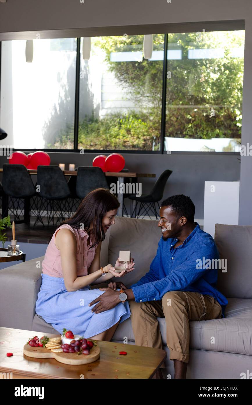 Ein Paar, das zu Hause die Verlobung feiert, eine Frau, die einen Ring hält, beide lächeln warm Stockfoto