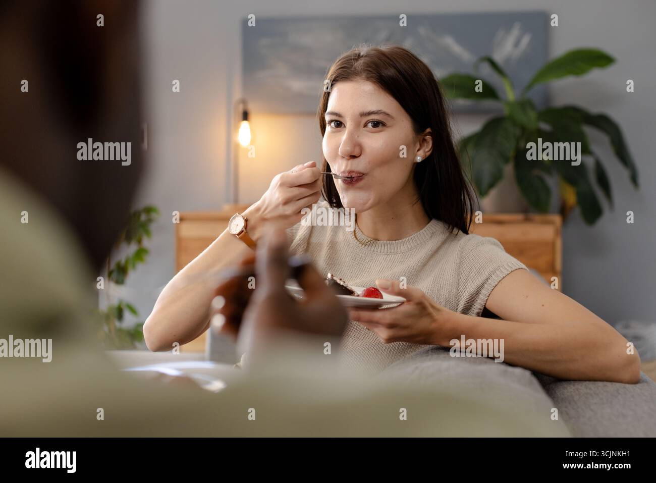 Frau genießt Nachtisch zu Hause, lächelt und sieht beim Essen zufrieden aus Stockfoto