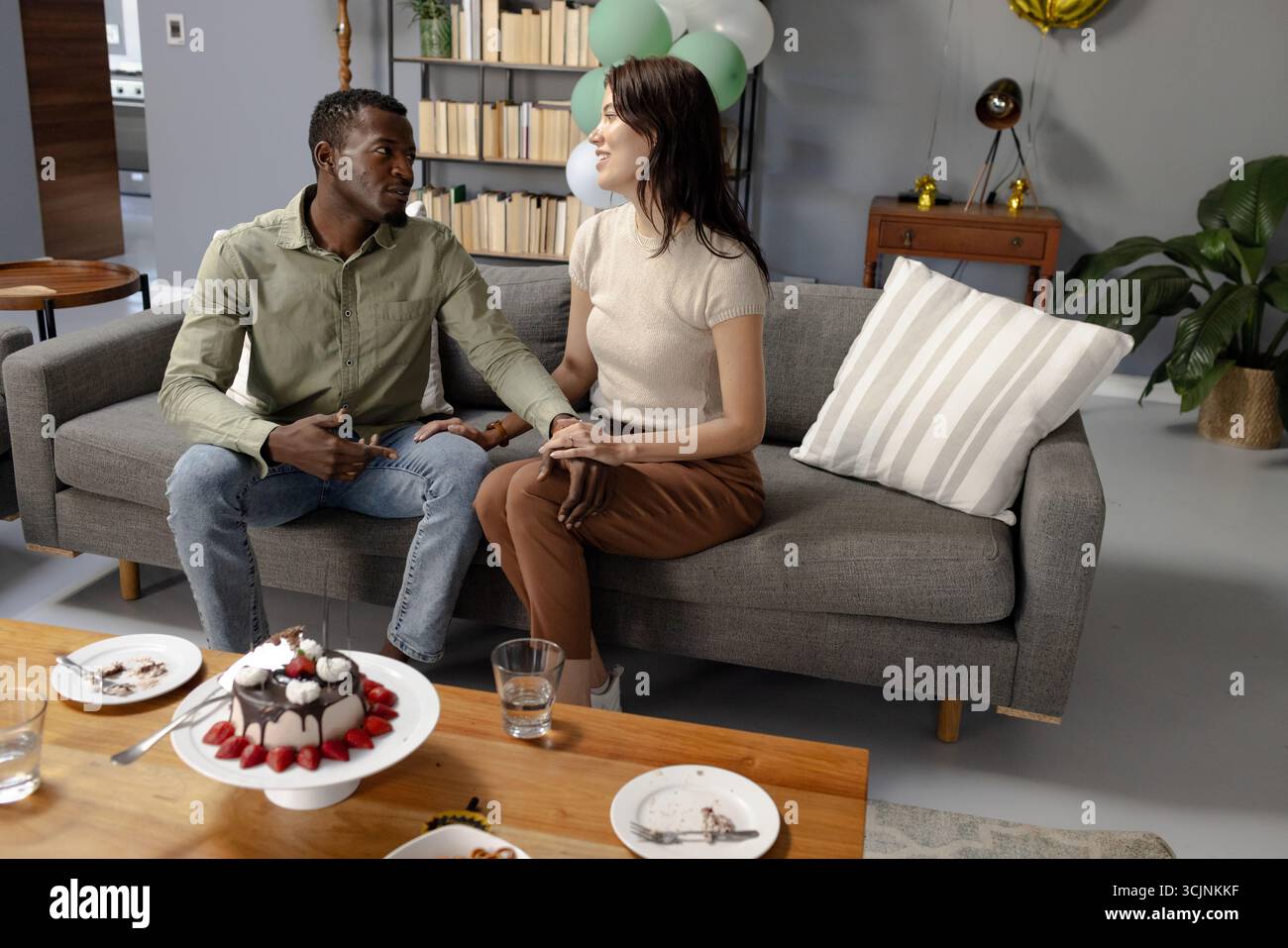 Paare, die auf dem Sofa sitzen und Hände halten, feiern mit Kuchen im Wohnzimmer Stockfoto