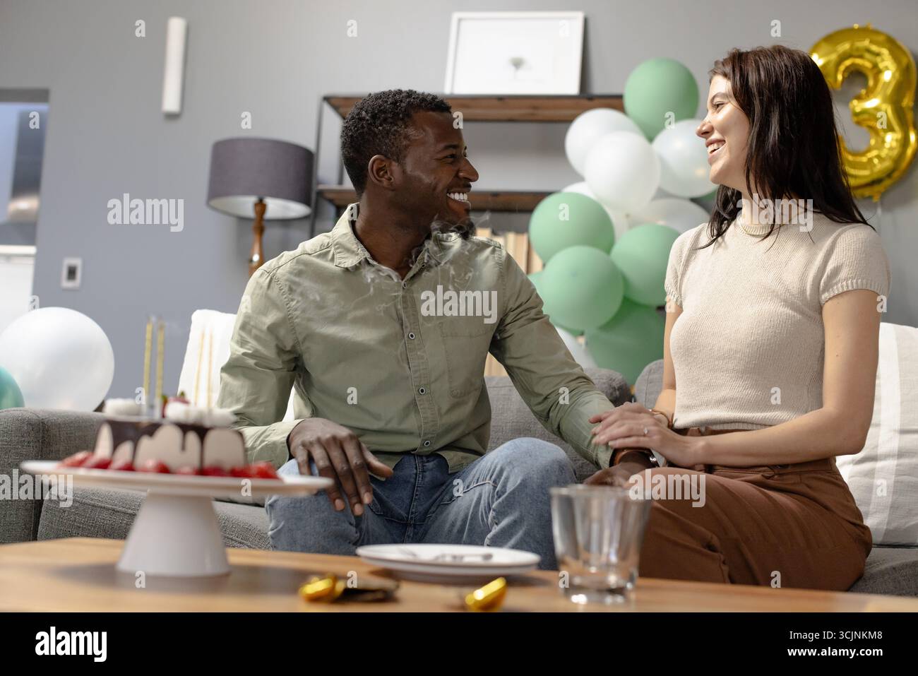 Ein Paar feiert zu Hause Geburtstag, lächelt und genießt Kuchen auf dem Sofa Stockfoto