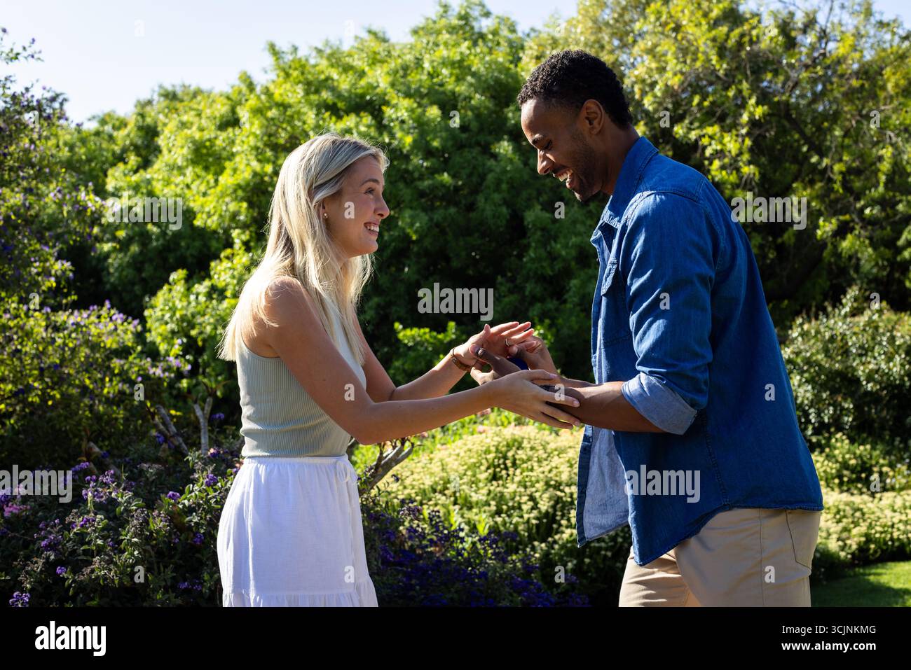 Feiert die Verlobung, ein Paar, das Lächeln und Lachen im sonnigen Garten tauscht Stockfoto