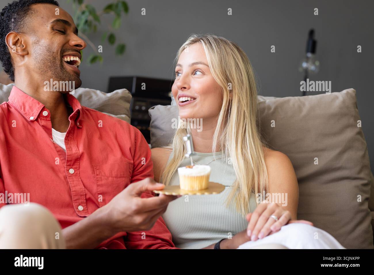 Ein Paar lacht und genießt Cupcake zusammen auf einer gemütlichen Couch zu Hause Stockfoto
