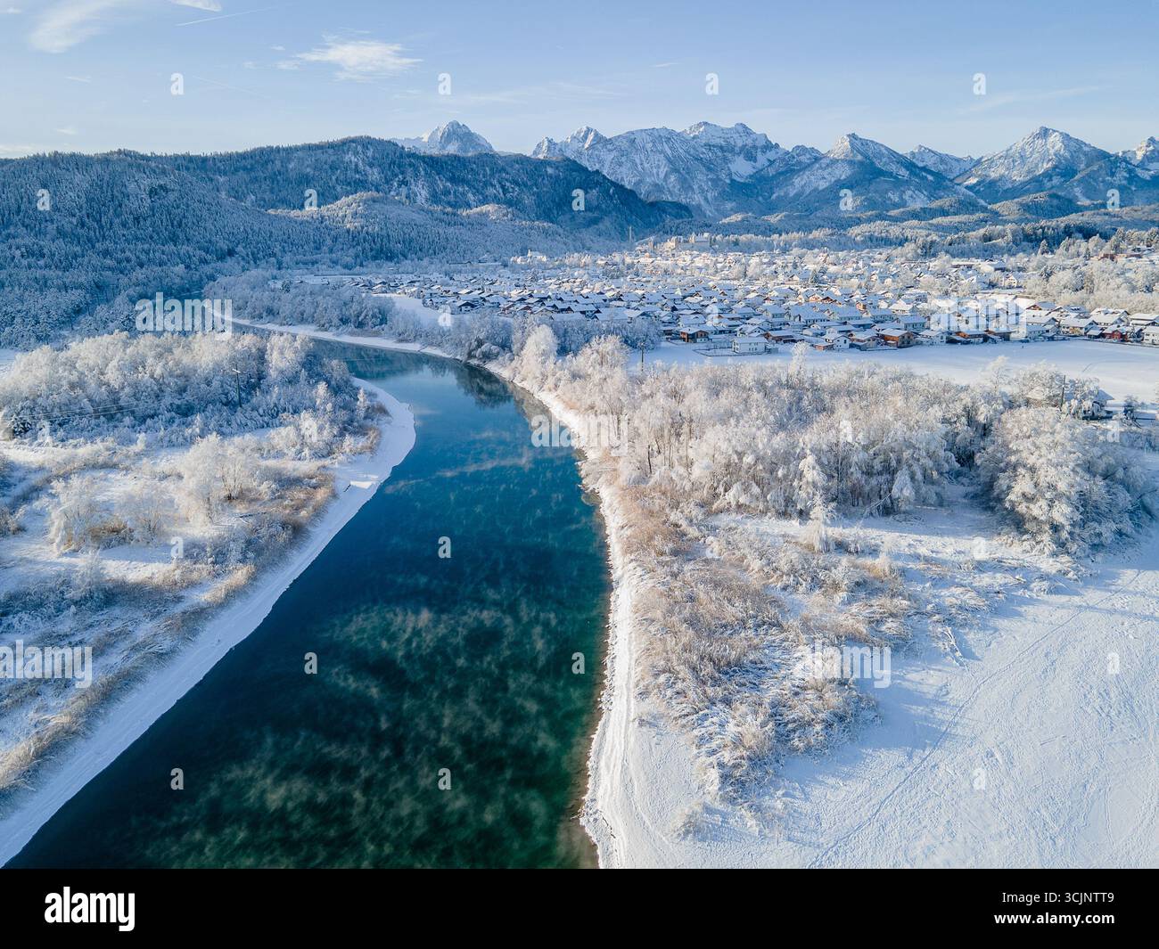 Aus der Vogelperspektive eines ruhigen Flusses, der durch eine schneebedeckte Landschaft in der Nähe der fernen Berge in Füssen, Bayern, Deutschland schneidet. Stockfoto