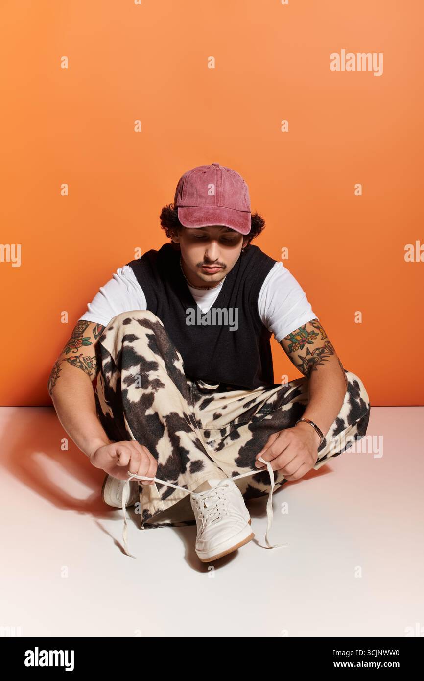 Hübscher junger Mann in modischer Kleidung sitzt auf dem Boden und bindet seine Schuhe stilvoll. Stockfoto