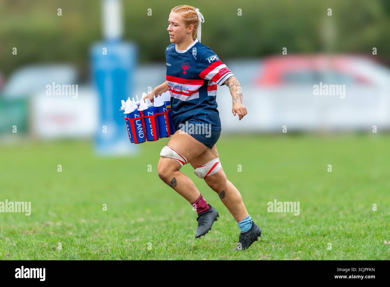 Eine Rugby-union-Spielerin, die eine Kiste mit Plastikflaschen aus Neuseeland trägt. Stockfoto