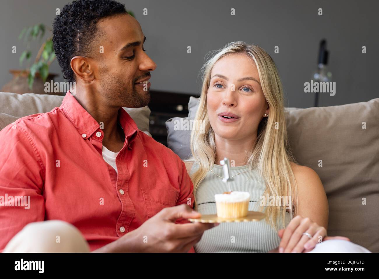 Ein Paar feiert zu Hause und genießt Cupcake mit fröhlichem Ausdruck auf dem Sofa Stockfoto