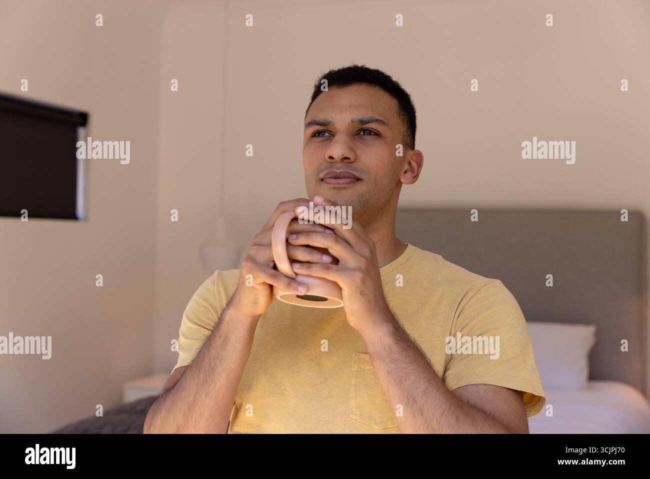 Junger Mann, der morgens Kaffee zu Hause genießt, nachdenklich und entspannt aussieht Stockfoto