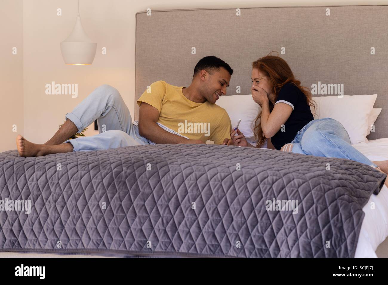 Ein junges Paar lacht und entspannt sich zu Hause auf dem Bett und genießt Gespräche Stockfoto