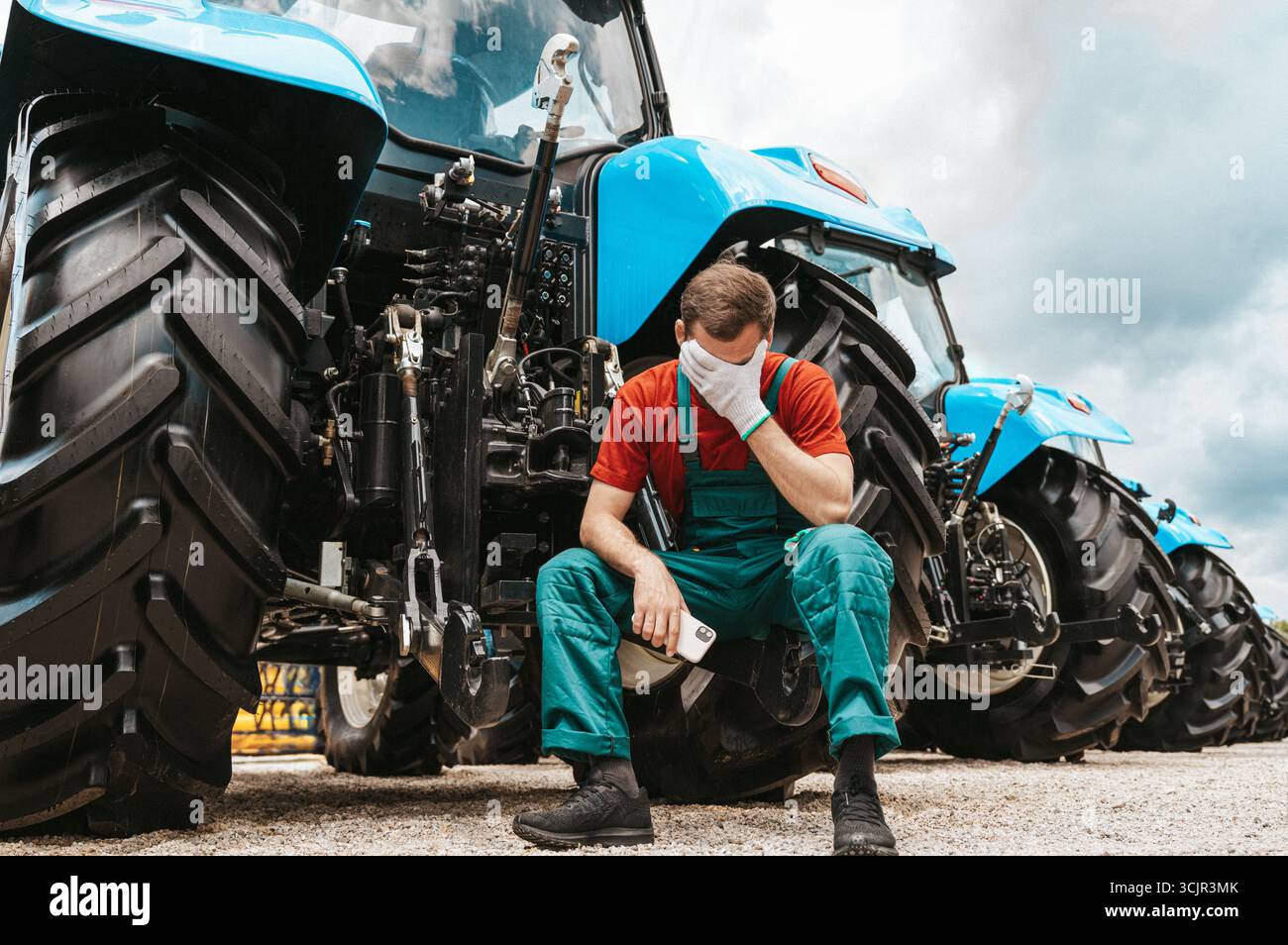 Trauriger und müder männlicher Landwirt, der bei Traktoren sitzt Stockfoto