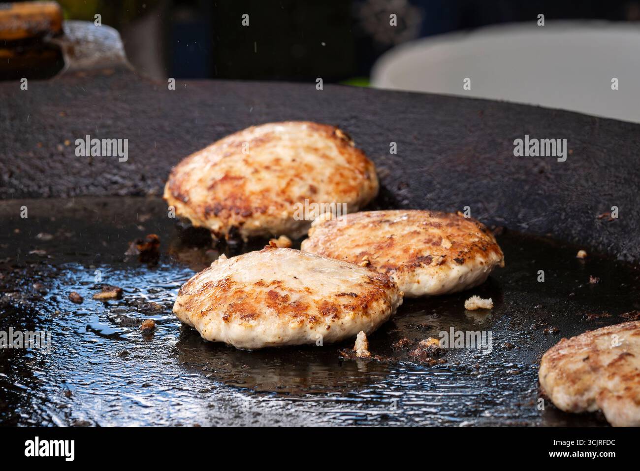 Auf einem großen runden Grill werden Fischpatties gebraten. Frisches Fischkotelett in einem Bratpfannengrill. Grillfest im Stadtpark. Street Fast Food. Stockfoto