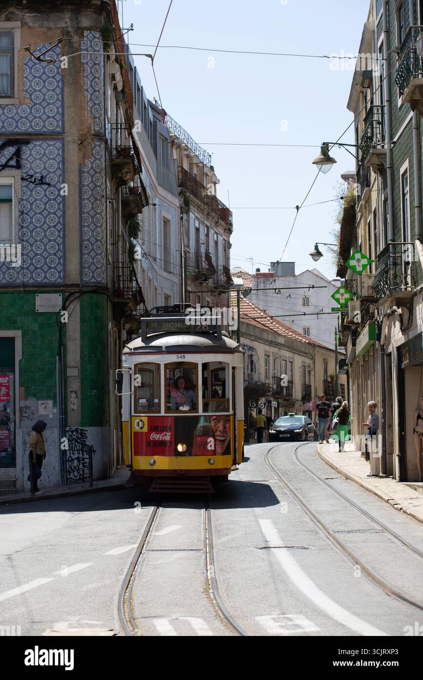 Lissabon, Portugal - Gelber und roter Trolley fährt eine Straße hinunter. Der Trolley wird für Coca-Cola geworben Stockfoto