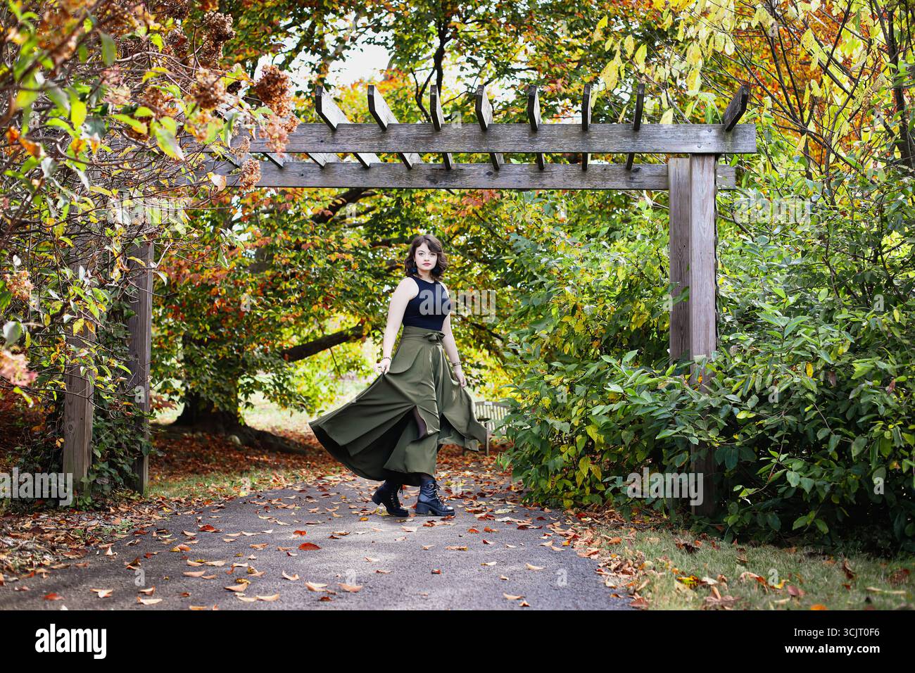 Schöne junge Frau unter einer Laube, Rock, der an den Beinen wirbelt, in einem Park mit verschwommenem Hintergrund von schönen Herbstfarben. Stockfoto