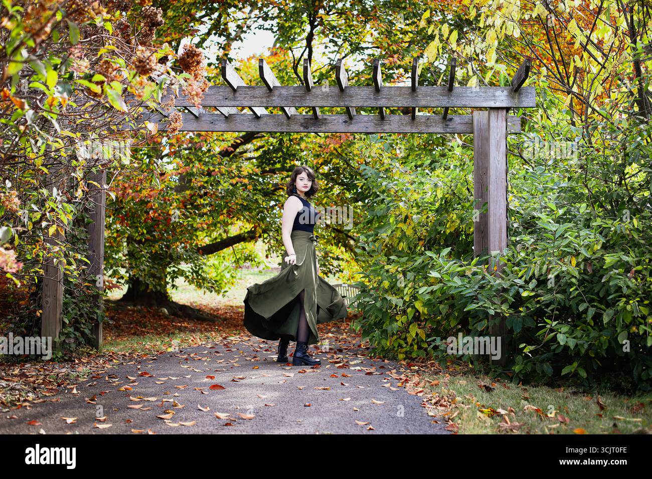 Schöne junge Frau unter einer Laube, Rock, der an den Beinen wirbelt, in einem Park mit verschwommenem Hintergrund von schönen Herbstfarben. Stockfoto