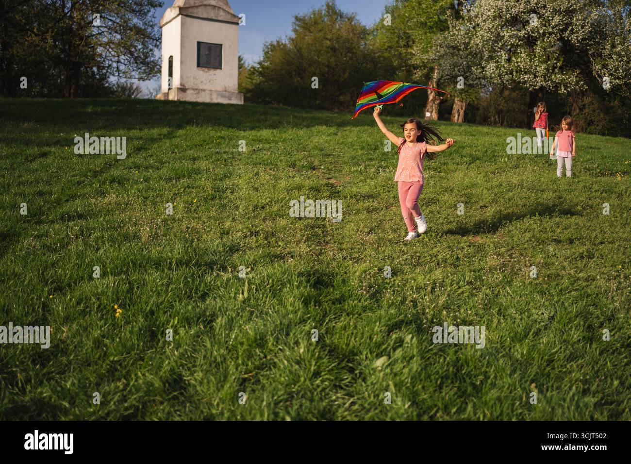 Kind, das fröhlich mit einer bunten Flagge auf einem sonnigen Hügel herumwirbelt Stockfoto