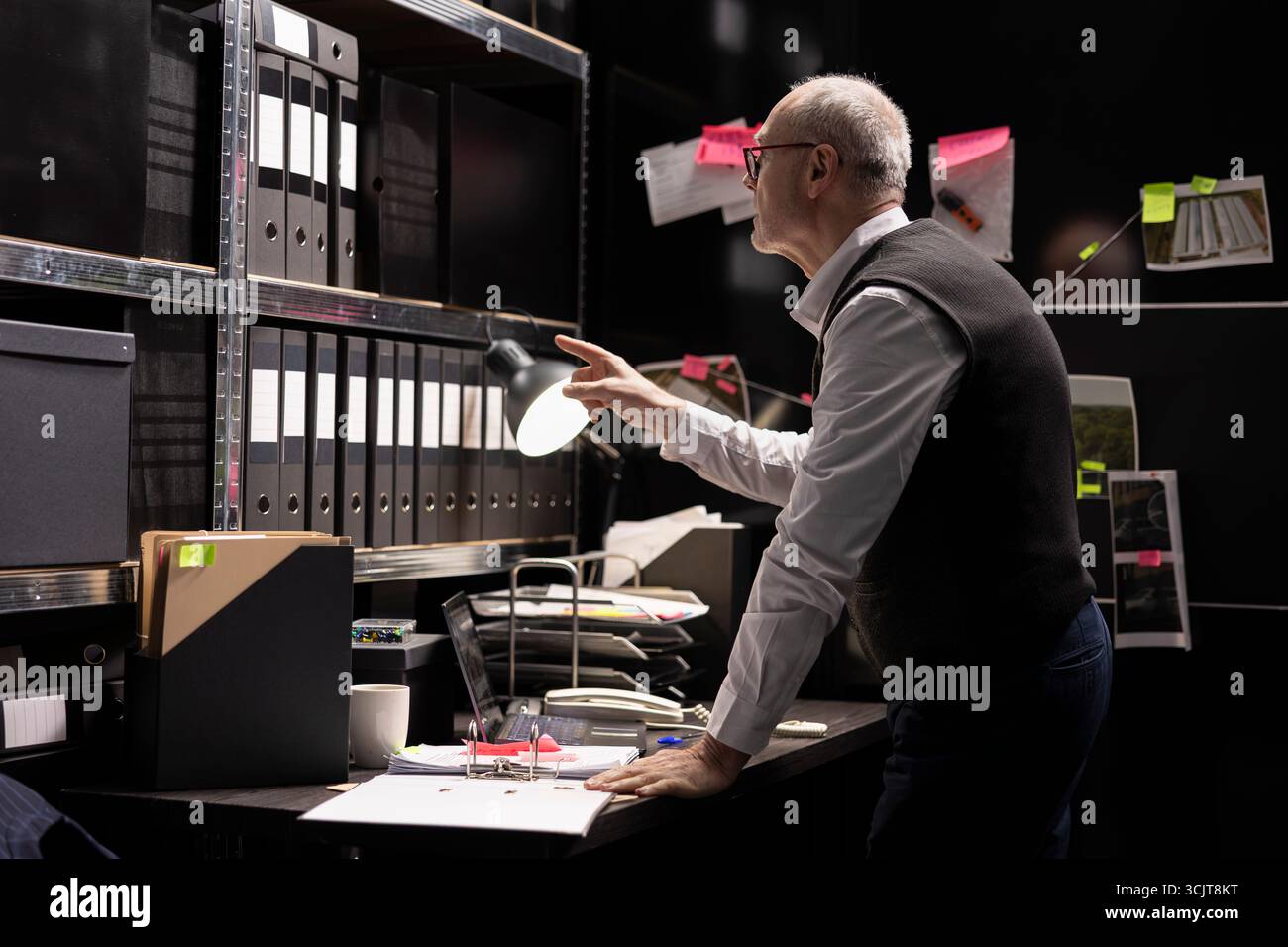 Ein alter Detective im Dienst in einem Beweisraum der Strafverfolgungsbehörde, sammelt Informationen und analysiert Akten, um illegale kriminelle Aktivitäten aufzuklären. Hinweise für die Untersuchung verknüpfen. Stockfoto