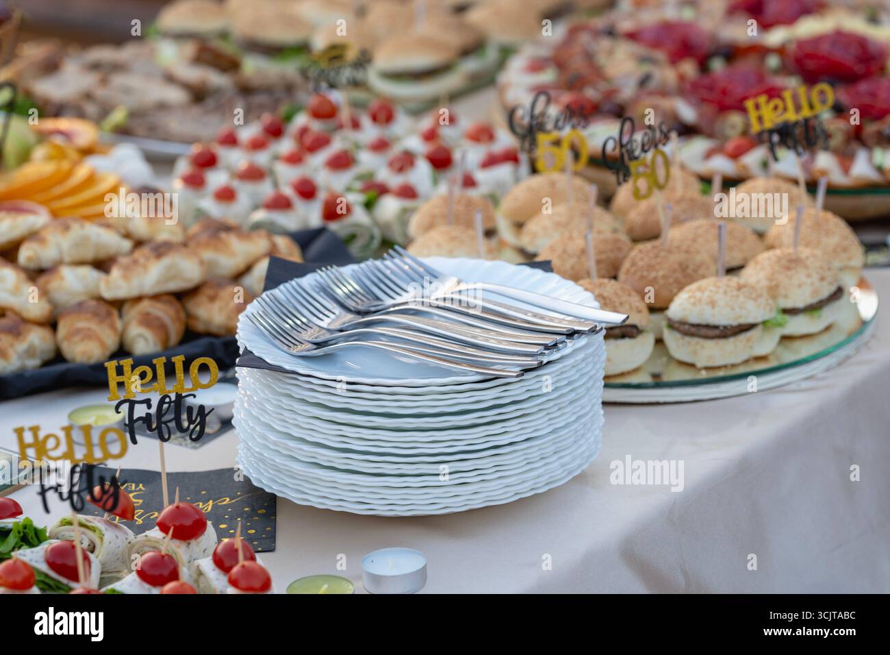 Weiße Teller mit Besteck und serviertem Essen – Catering-Setup für die Geburtstagsfeier Stockfoto