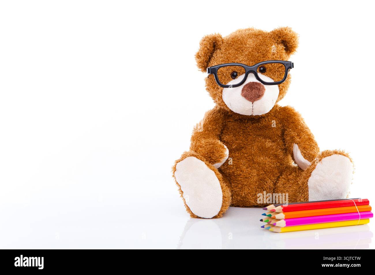 Sitzender Teddybär mit Brille und Buntstiften Stockfoto