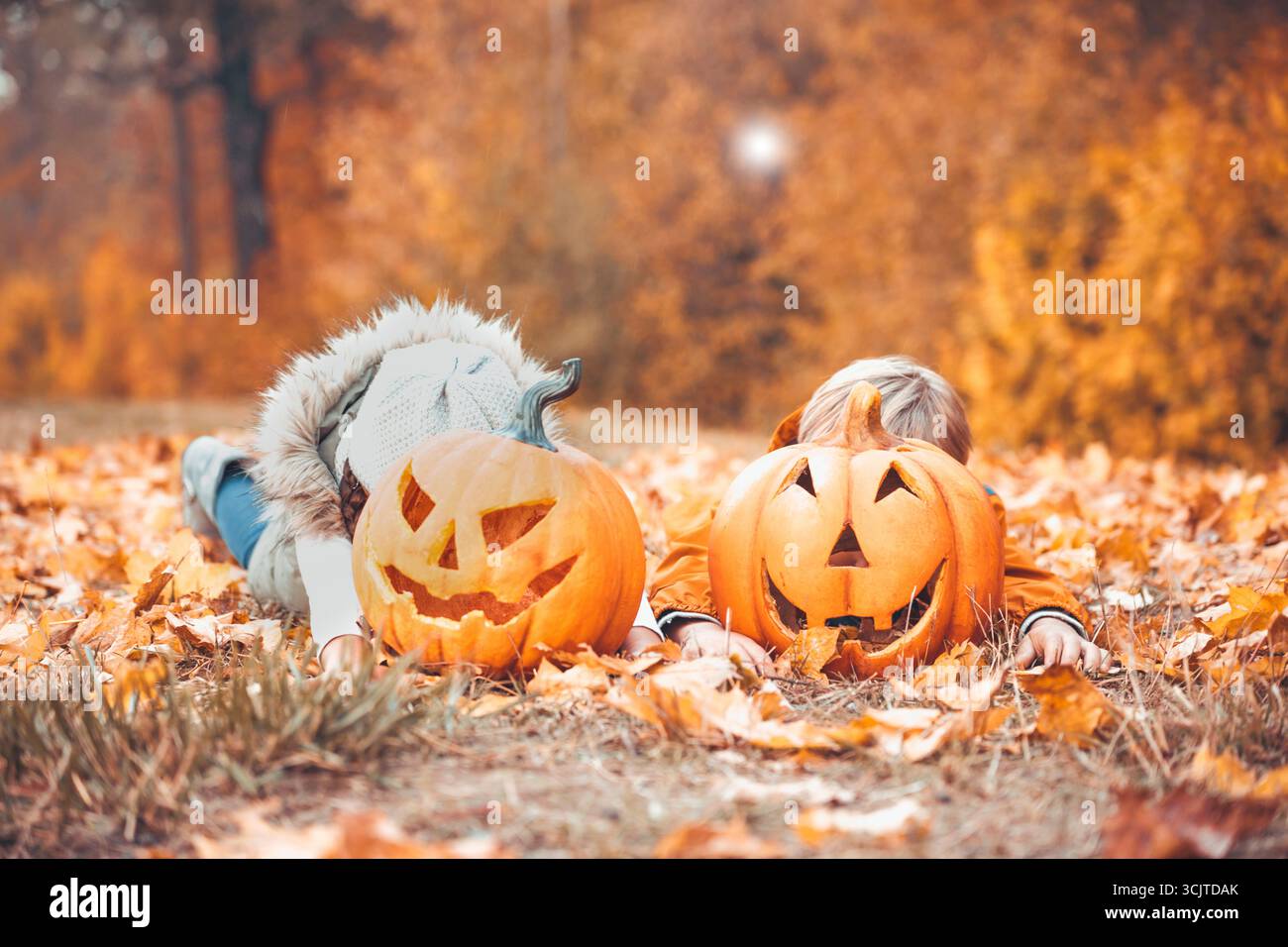 Zwei Kinder, die sich im Herbst hinter Halloween-Kürbissen verstecken Stockfoto