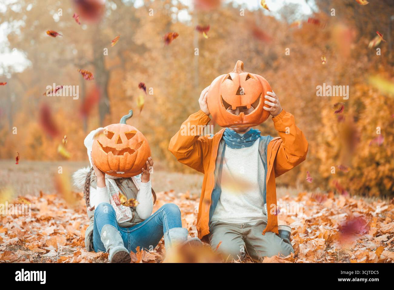 Zwei Kinder, die sich im Herbst hinter Halloween-Kürbissen verstecken Stockfoto