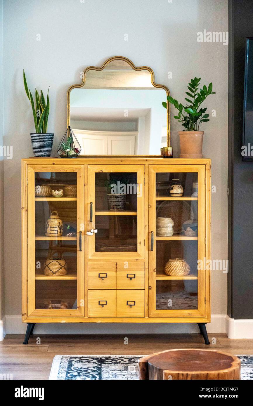 In einem gemütlichen Wohnzimmer befindet sich ein Holzschrank mit einem Spiegel darüber Stockfoto