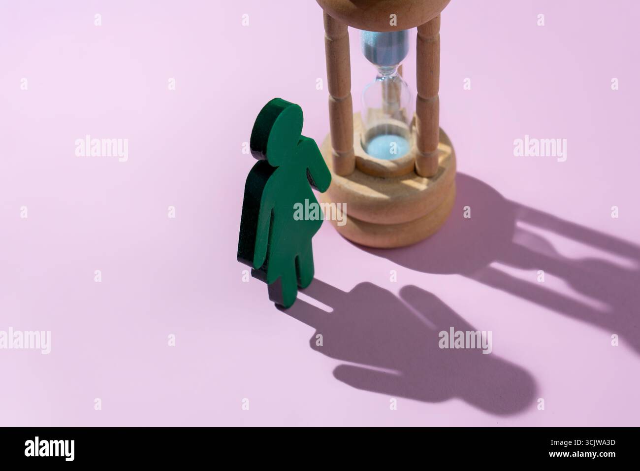 Figur einer Frau, die neben einer hölzernen Sanduhr steht. Weibliches Altern, biologische Uhr, Fruchtbarkeit, Lebensstadien eines Frauenkonzepts. Stockfoto