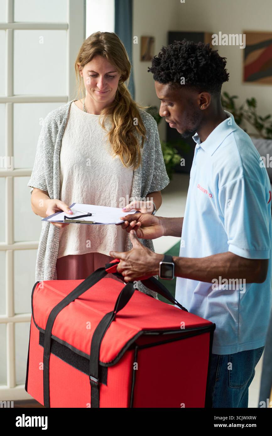 Frau, die das Lieferformular mit dem Black man Courier im Haus überprüft Stockfoto