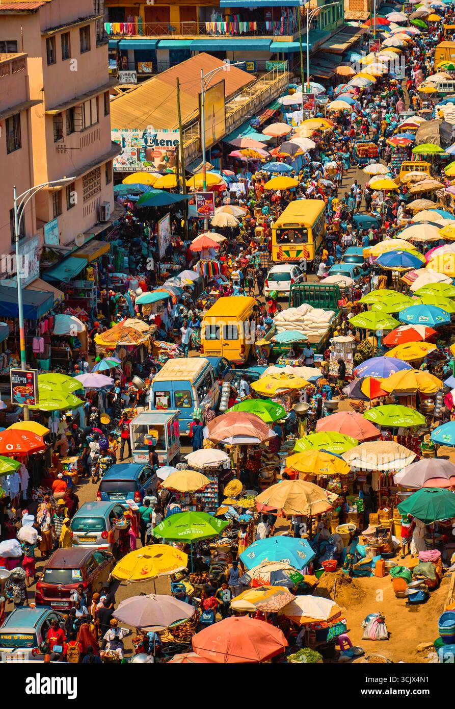 Accra, Ghana - 5. November 2022: Aus der Vogelperspektive das lebhafte Chaos des Makola Markts, ein dichter Wandteppich aus bunten Regenschirmen, die die geschäftigen Menschenmassen beschatten, und gelbe Busse, die durch die geschäftigen Straßen fahren. Stockfoto