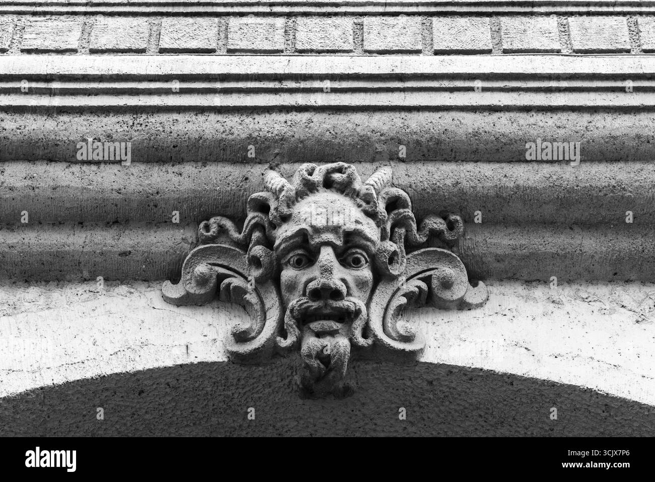 Architektonische Steinschnitzerei eines dekorativen Gesichts mit detaillierten Details, einfarbig erfasst. Das kunstvolle Design unterstreicht das künstlerische Handwerk Stockfoto Architektonische Steinschnitzerei eines dekorativen Gesichts mit detaillierten Details, einfarbig erfasst. Das kunstvolle Design unterstreicht das künstlerische Handwerk Stockfoto