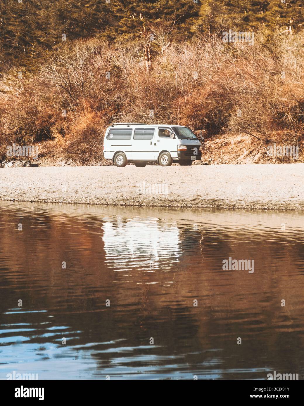 Saiko Lake, Japan - 28. Februar 2025: Blick auf einen weißen Van, der am Ufer geparkt ist, dessen Reflexion im stillen Wasser des Sees schimmert. Stockfoto