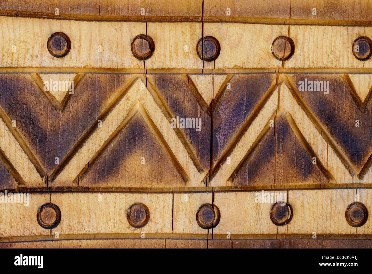 Detaillierte Ansicht einer Holzoberfläche mit geschnitzten geometrischen Verzierungen einschließlich Dreiecken und Kreisen, die traditionelle Handwerkskunst und strukturierte na zeigen Stockfoto