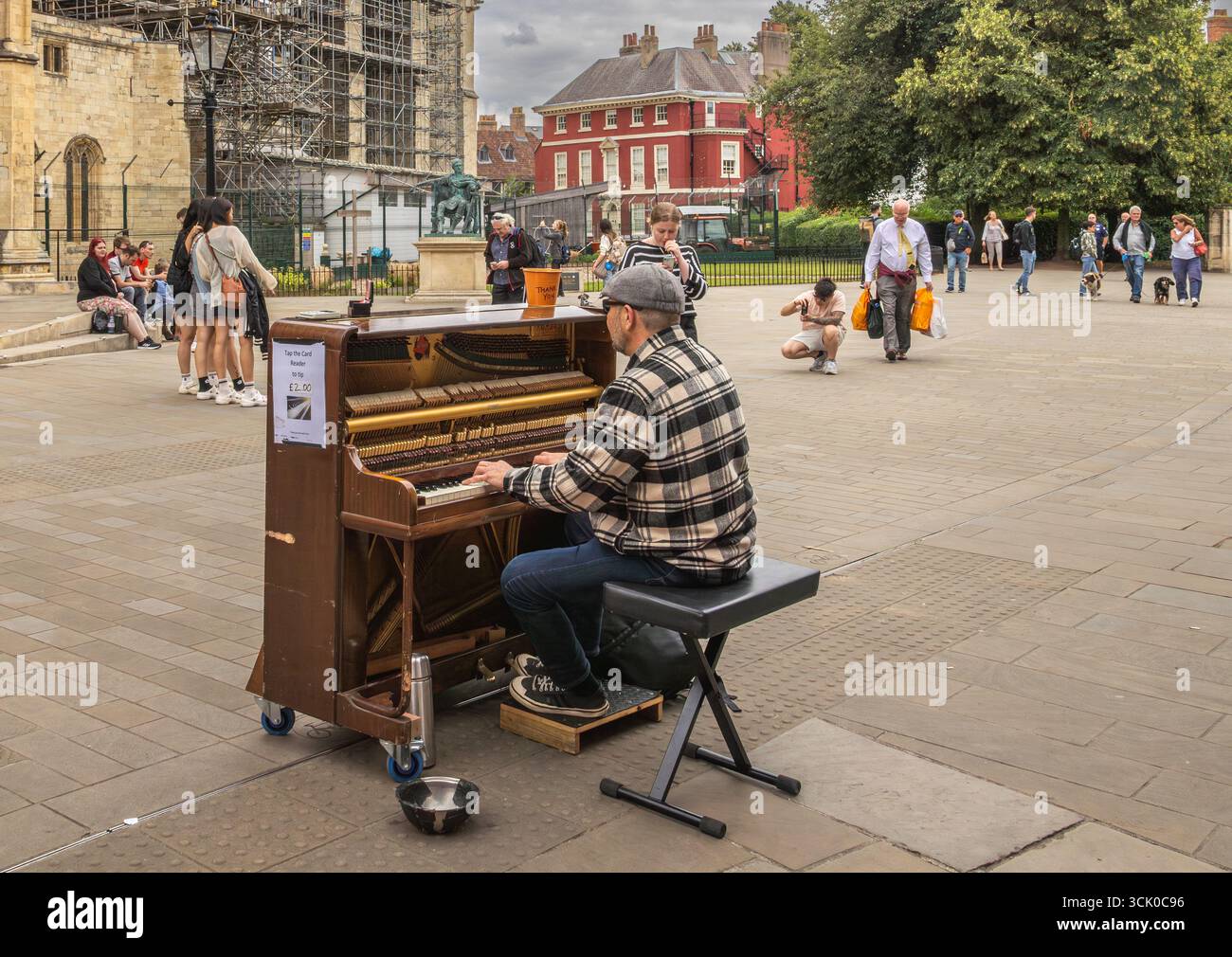 Straßenkünstler spielt Klavier auf einem öffentlichen Platz in York, England, mit Trinkglas, Publikumsinteraktion und historischer Architektur im Hintergrund Stockfoto