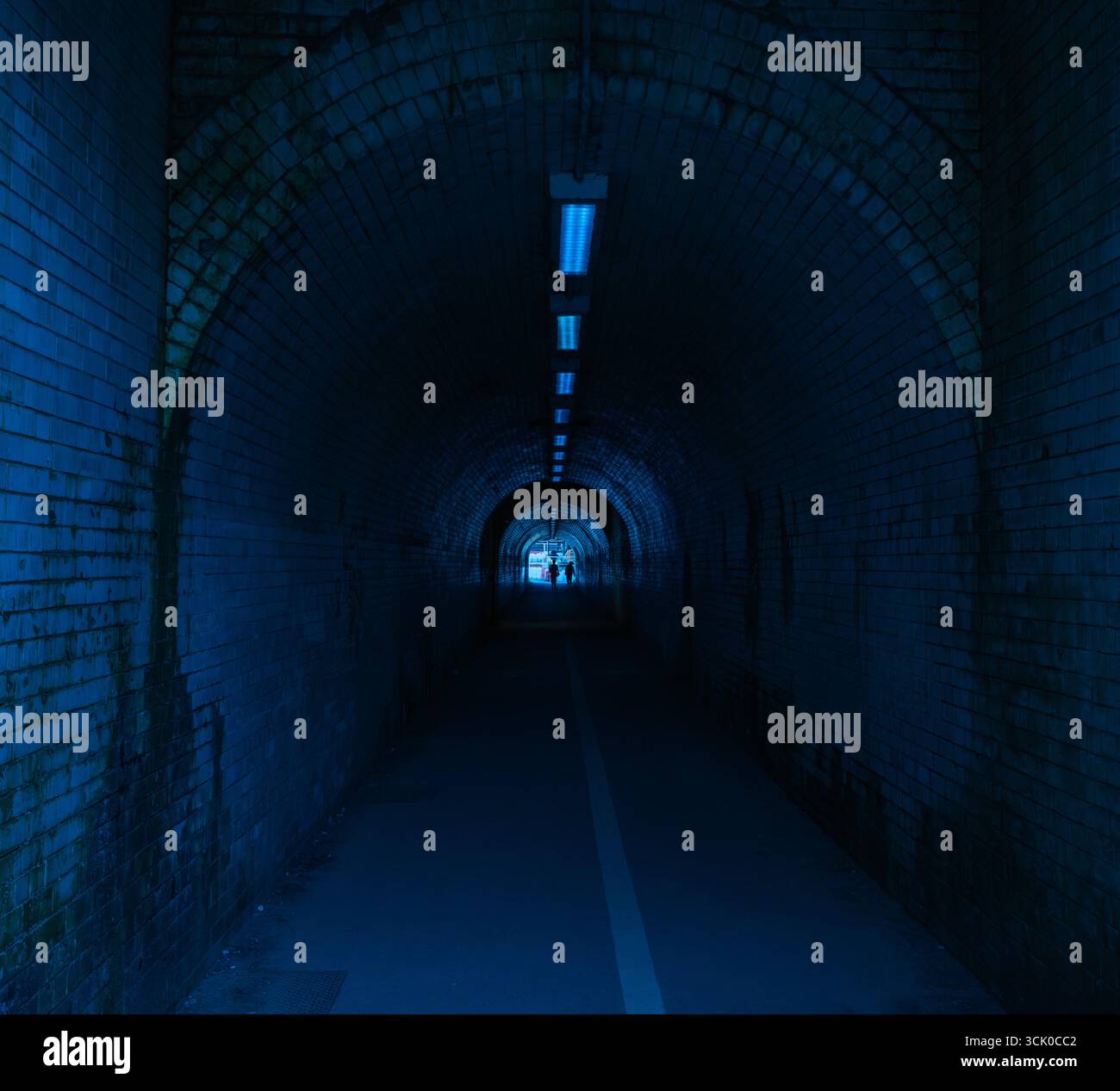 Stimmungsvoller Backsteintunnel mit blauer Beleuchtung und geschwungener Decke, der Themen der Isolation, des Übergangs und der architektonischen Symmetrie weckt Stockfoto