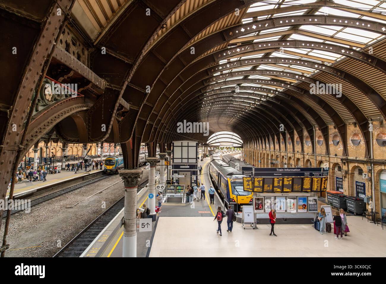 Passagiere steigen ein und navigieren durch Bahnsteige im Bahnhof York in England, eingerahmt von kunstvollen Eisenwerken, Bogendach und Digital Signage Stockfoto