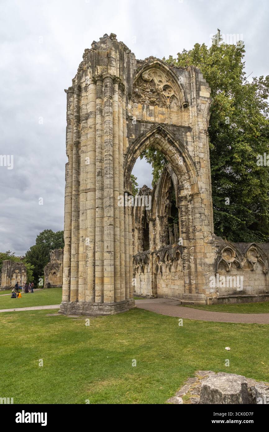 Ruinen der St. Mary’s Abbey in York Museum Gardens, England, mit gotischen Steinbögen und verwitterten Säulen, die über Gras und Bäumen ragen. Stockfoto
