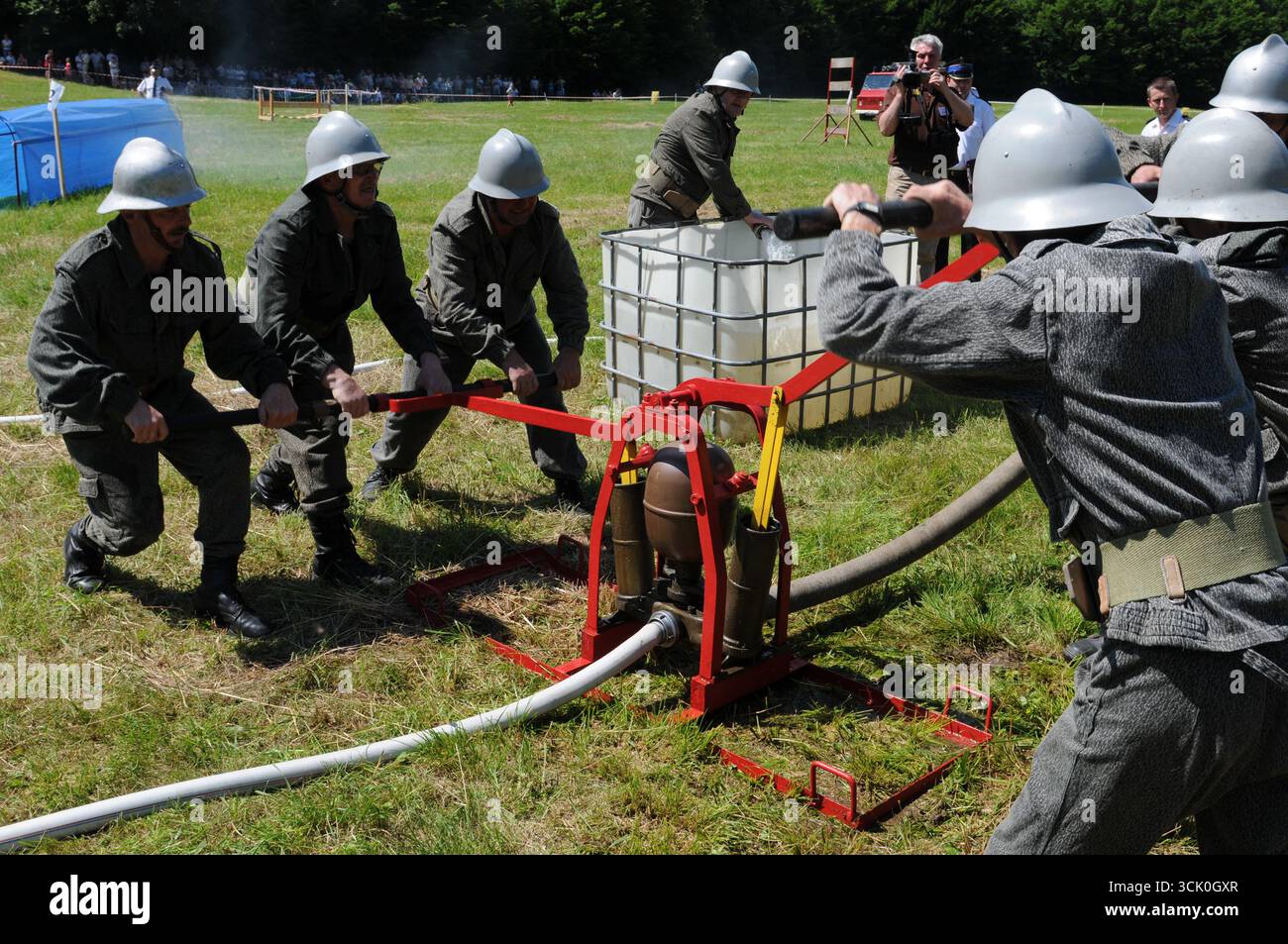 Feuerwehrleute in grauen Uniformen und weißen Helmen, die Handpumpen während des historischen Feuerwehrwettbewerbs in Rudawka Rymanowska, Subkarpaten, Pola betreiben Stockfoto