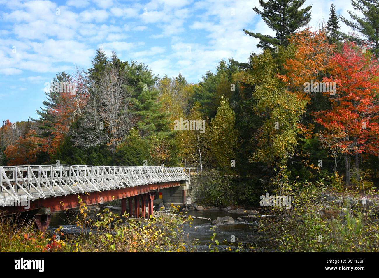Die rot-weiße Brücke überquert den Androscoggin River in New Hampshire. Der orangene Fall hinterlässt die Farbe gegenüber dem Ufer. Stockfoto
