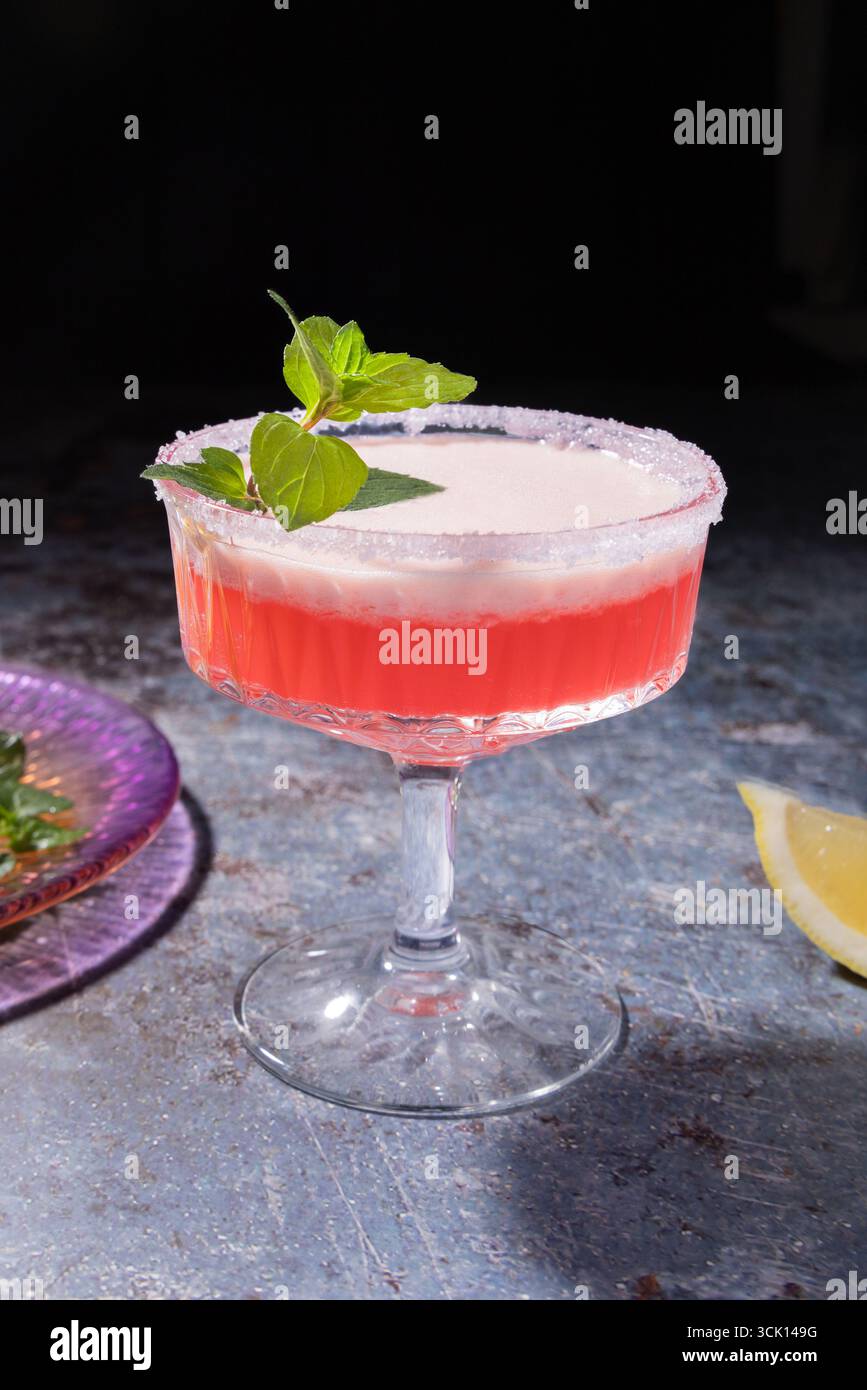 Eleganter Erdbeerdaiquiri mit Minzzweig und Zitronenkeil, serviert in einem gezuckerten Coupé-Glas – lebendig, erfrischend und sommerlich. Stockfoto