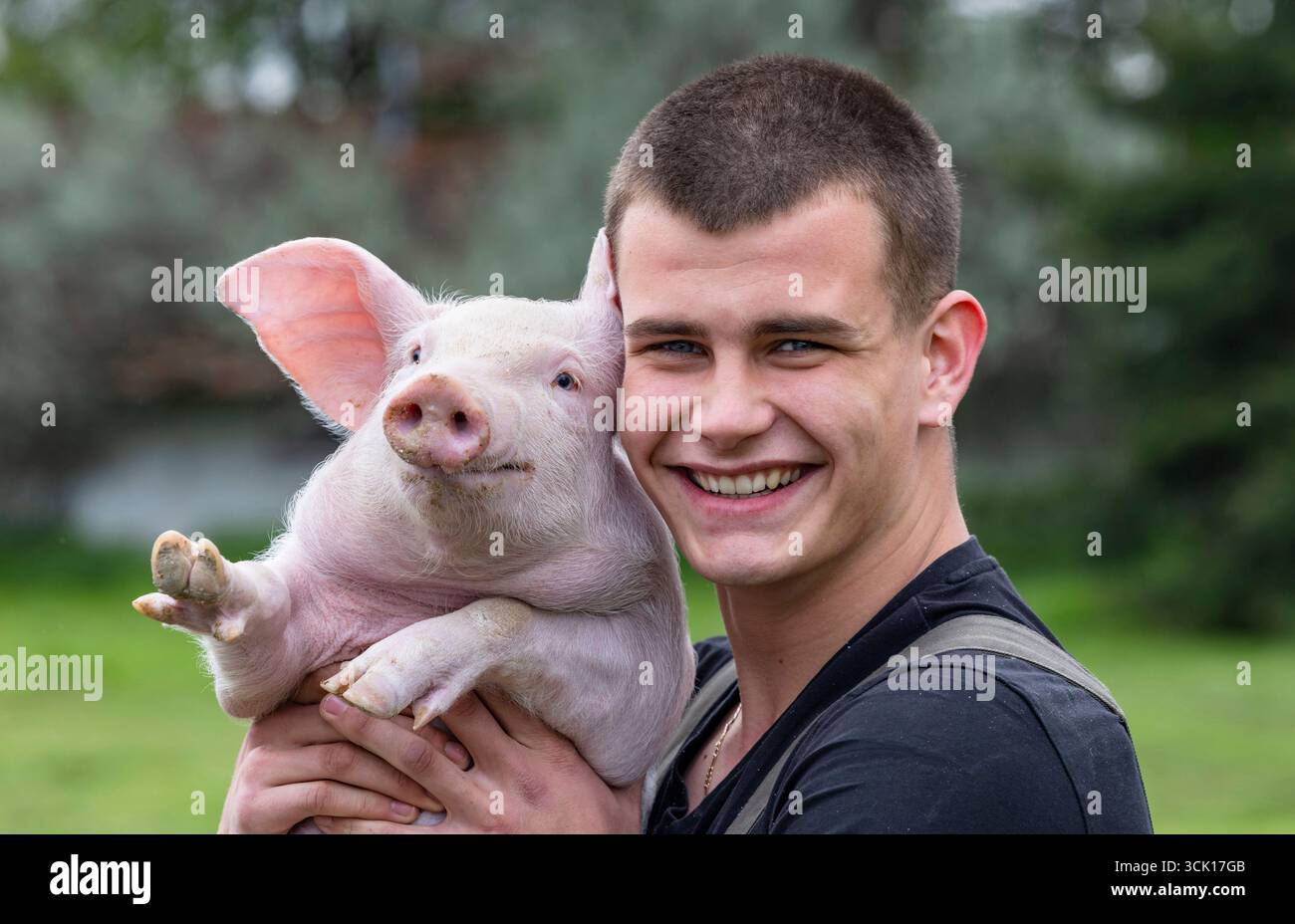 Porträt eines fröhlichen Bauern, der sich kuschelt und Ferkel hochhält, um einen süßen Moment zu teilen Stockfoto