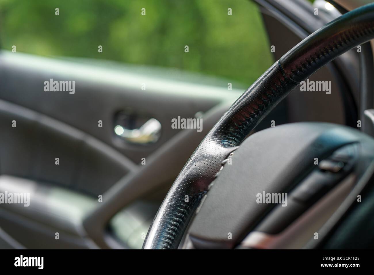 Ansicht eines schwarzen Fahrzeuglenkrads vor dem Hintergrund einer offenen Tür. Nahaufnahme eines Autolenkrads mit verschiedenen Tasten Stockfoto